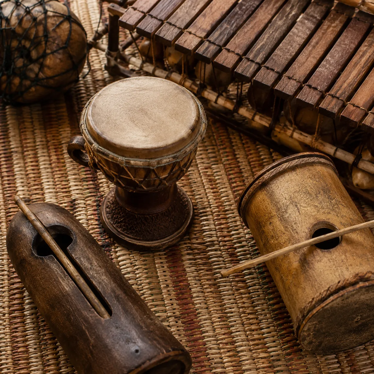 Traditional Angolan instruments including a dikanza scraper and ngoma drum on a reed mat